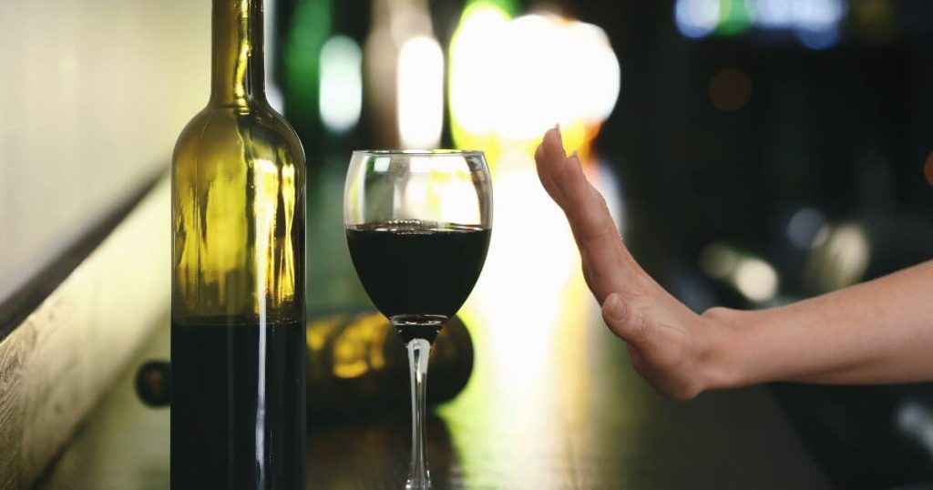 Hand gesturing to refuse a glass of red wine with a bottle on a bar counter, symbolizing abstinence and participation in Dry January for health and wellness.