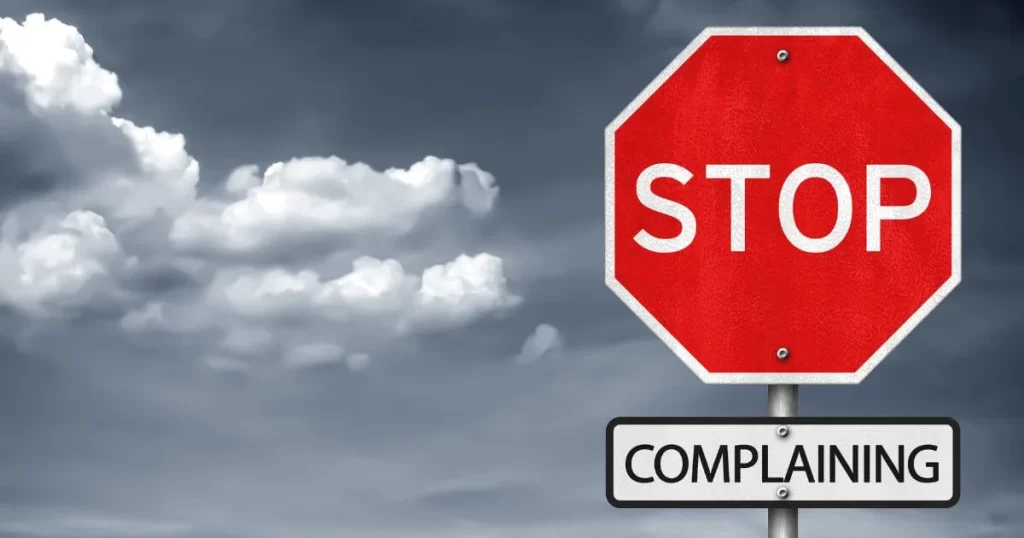 a stop sign with a 'complaining sign underneath in front of cloudy skies