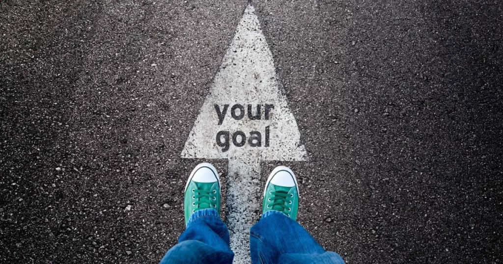 A POV shot of a pair of sneakers standing on top of an arrow that says your goals
