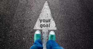 A POV shot of a pair of sneakers standing on top of an arrow that says your goals